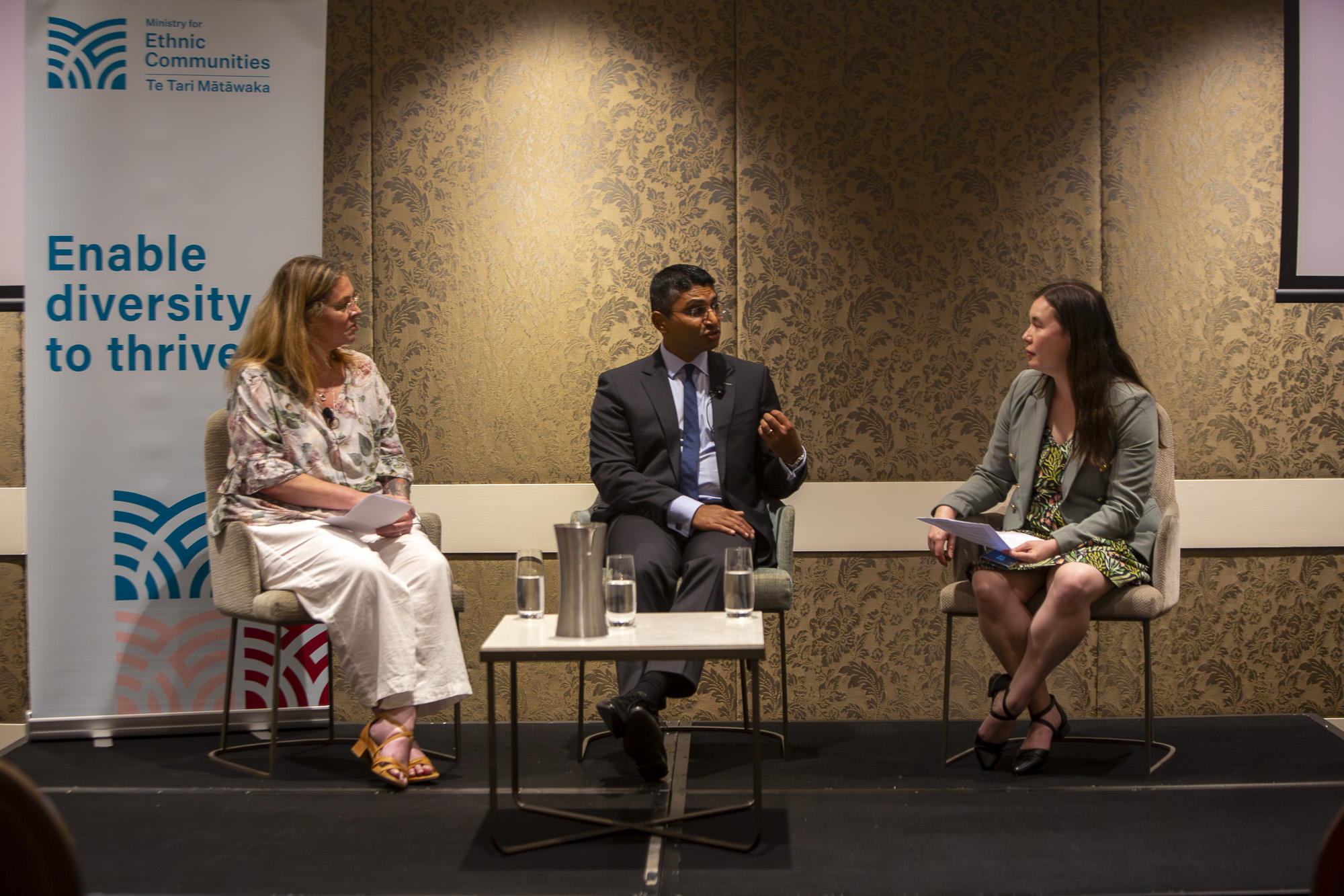 Three people sit on a stage talking to one another