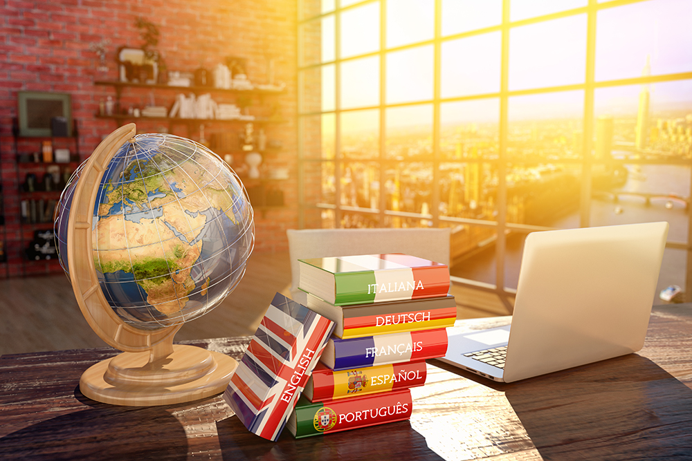 image of a desk with a globe on the left, various language dictionaries in the middle and a laptop on the right