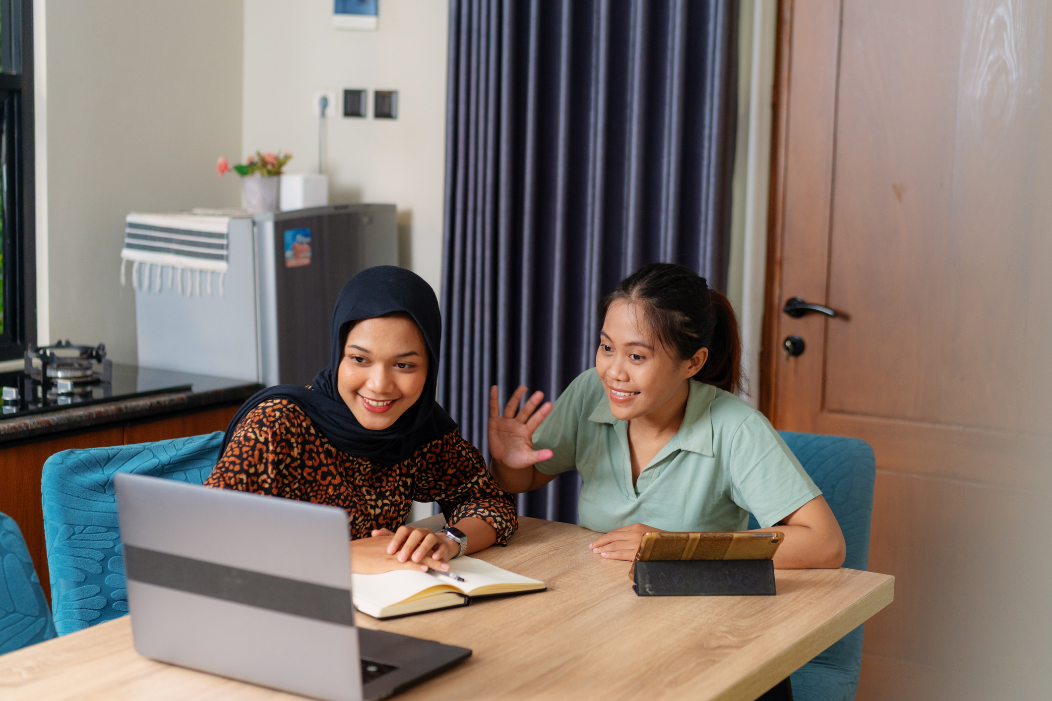 Image of 2 people sitting at a table talking to their laptop