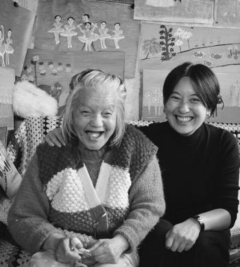 LanguageG whotoinclude 0 Black and white image of two women sitting in front of a wall of art.