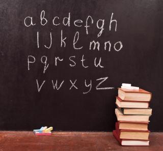 Image of blackboard with alphabet in chalk on it and a pile of books on the right.