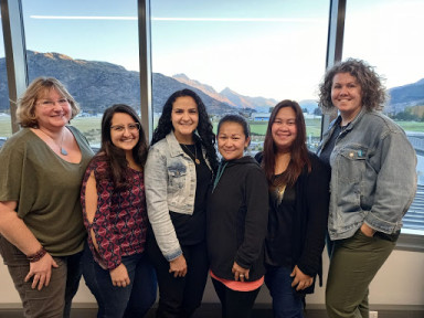 GoodYarn facilitators smiling and standing side by side in front of a window. Behind the window is a view of Queenstown.